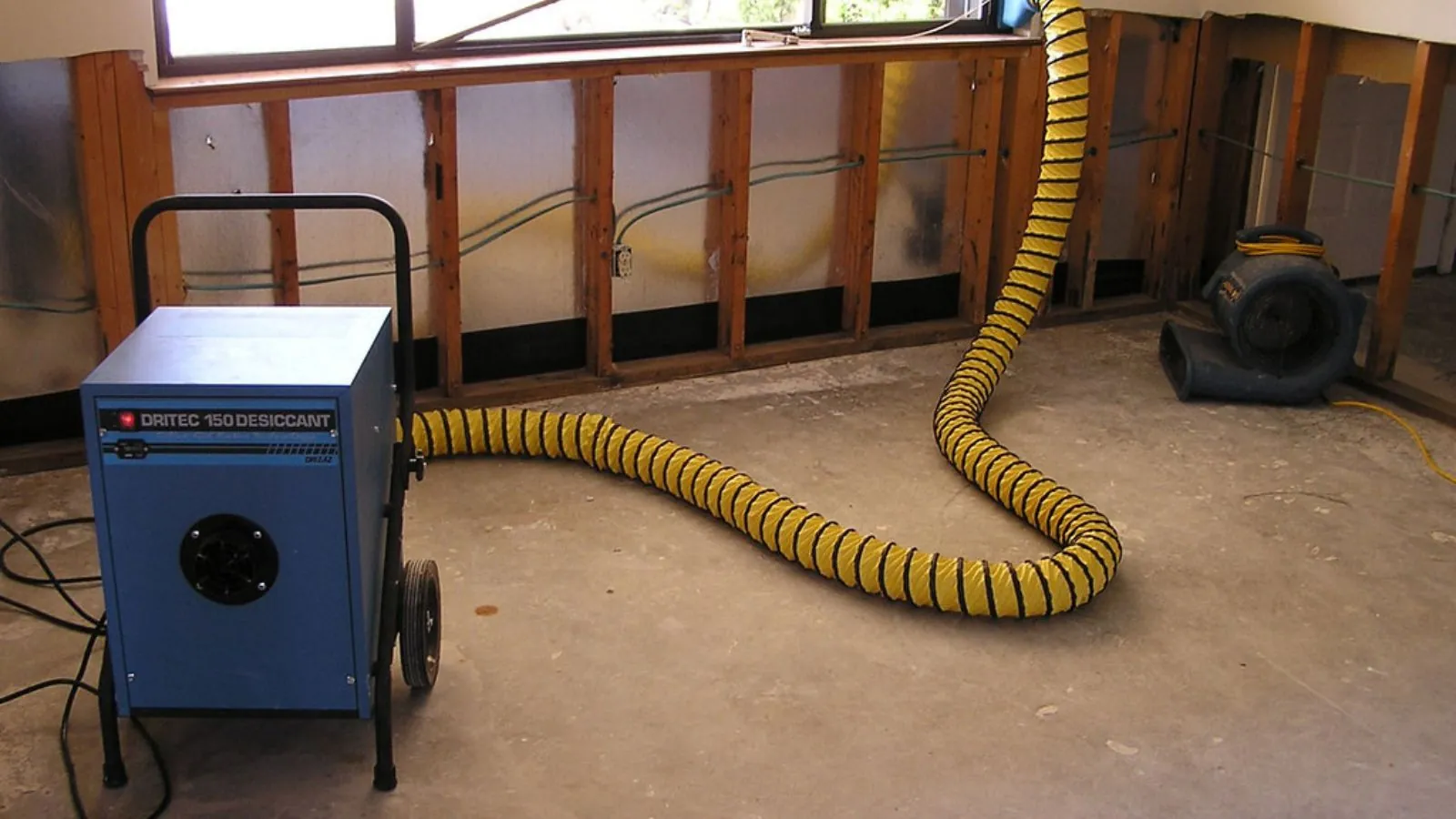 Dehumidifier with a yellow duct hose in a room with exposed wall framing