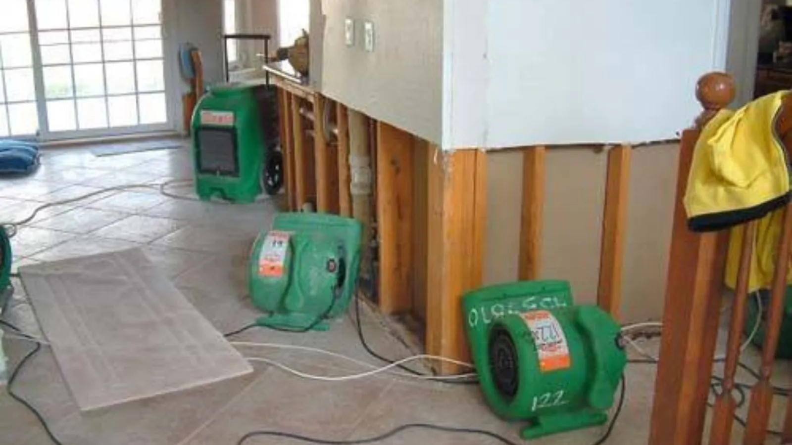 Green air movers and a dehumidifier in a room with wall sections cut out